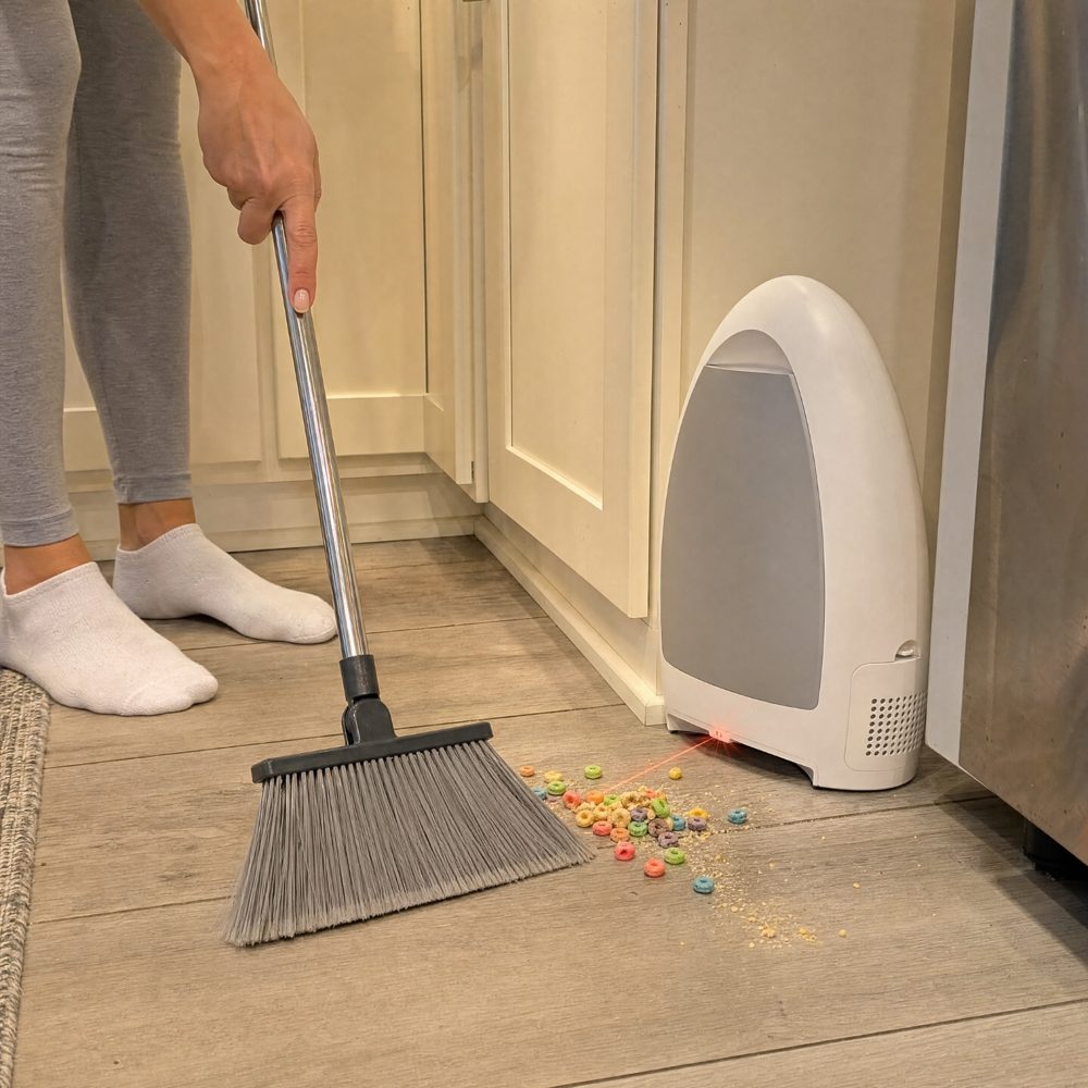 A person sweeping spilled cereal toward the EyeVac touchless vacuum in a kitchen
