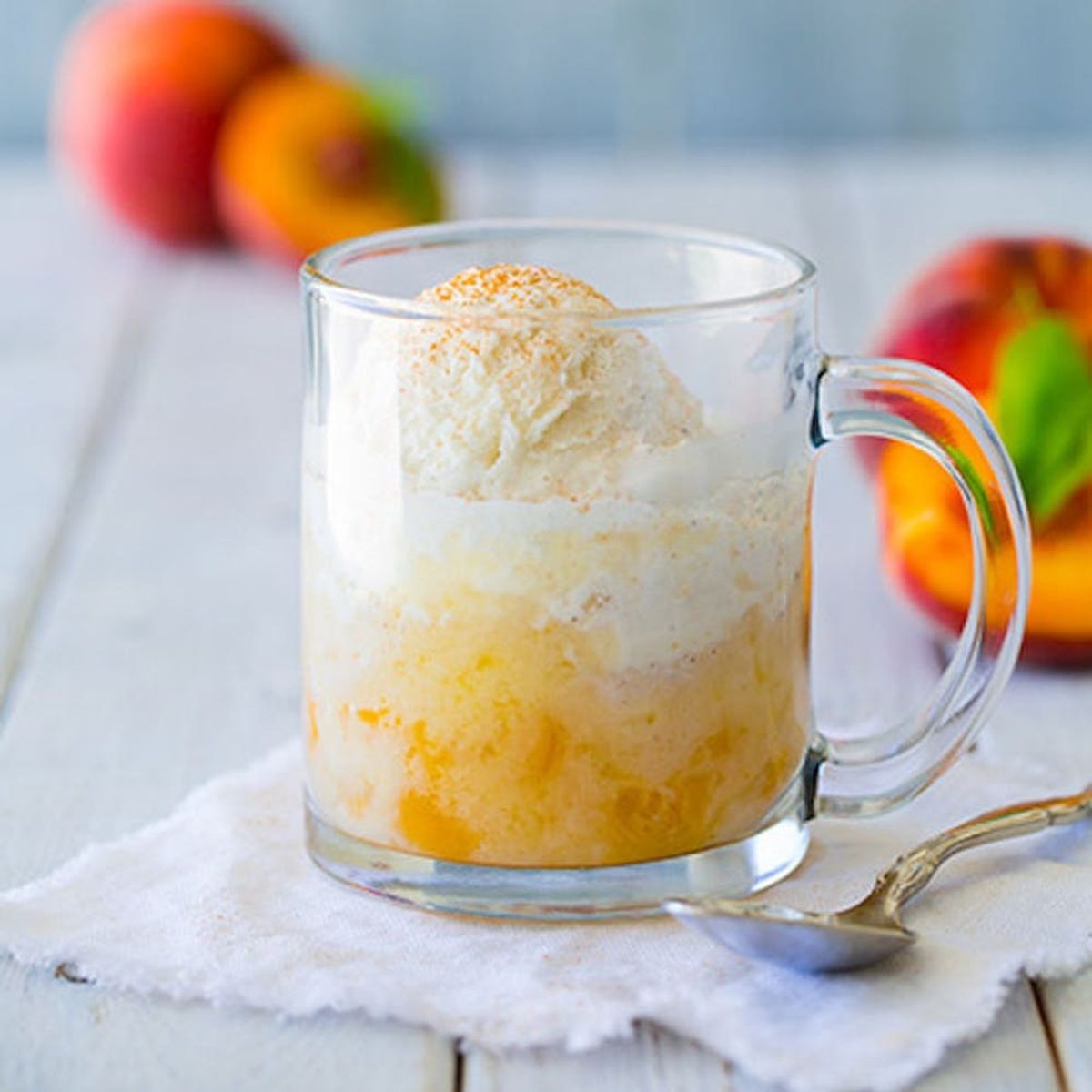 26 Delicious mug recipes worth exploring features this peach cobbler mug cake in a clear mug and silver spoon.