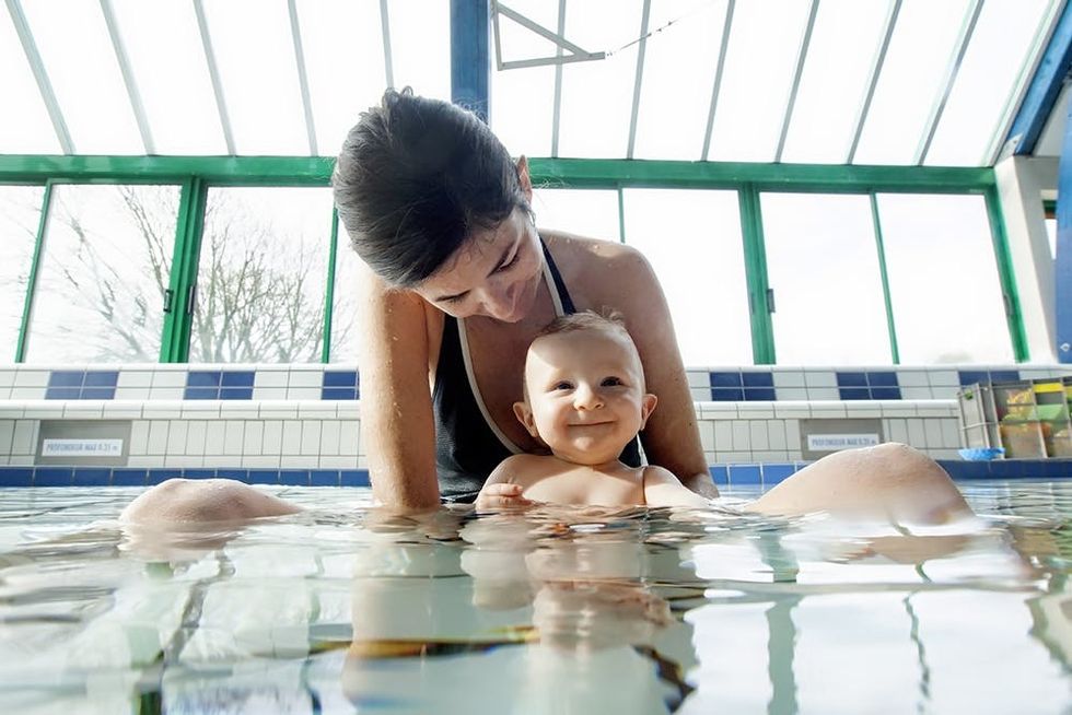 8 month old baby boy enjoying his first swim in a public swimming pool with his parents, Ploemeur, Brittany, France.