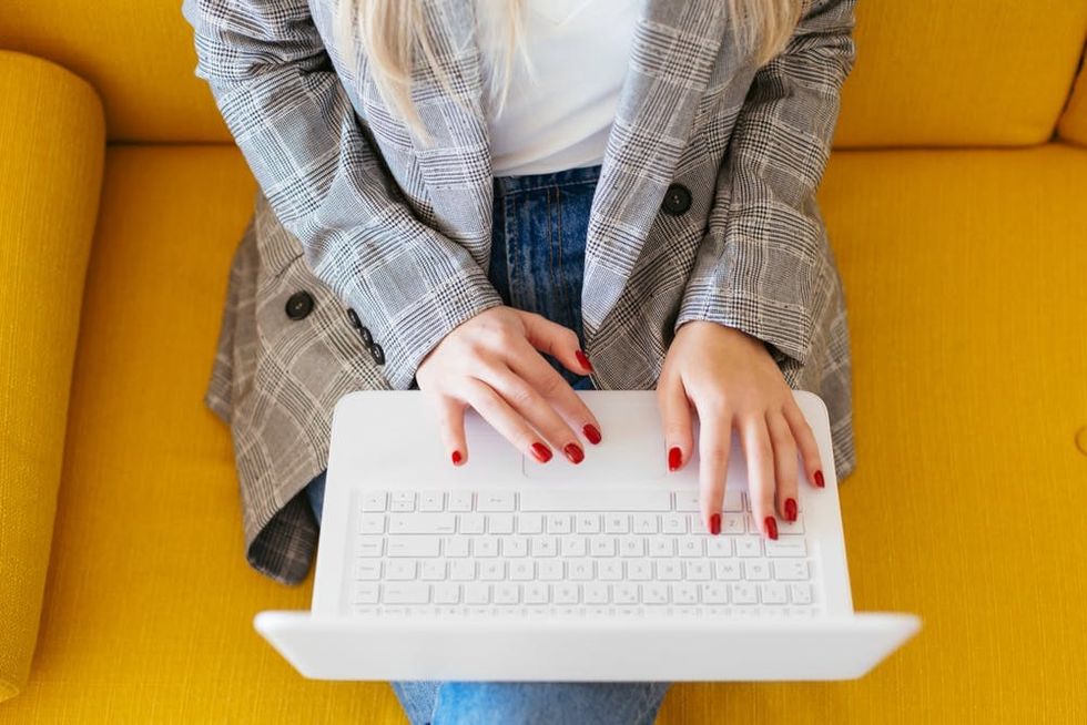 970157460 Businesswoman sitting on yellow couch, using laptop