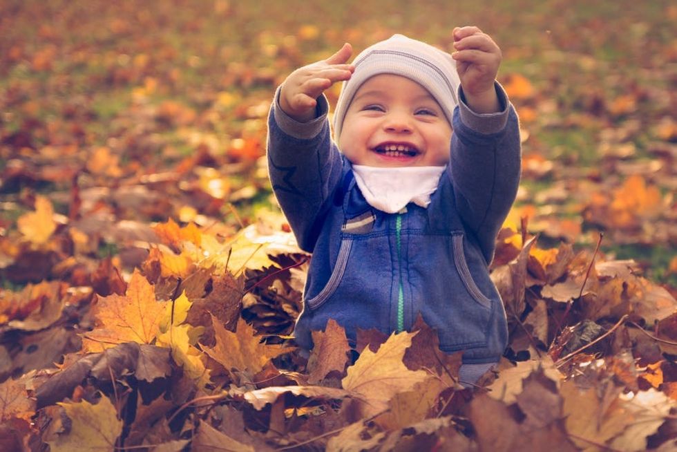 A baby happily plays in a pile of leaves