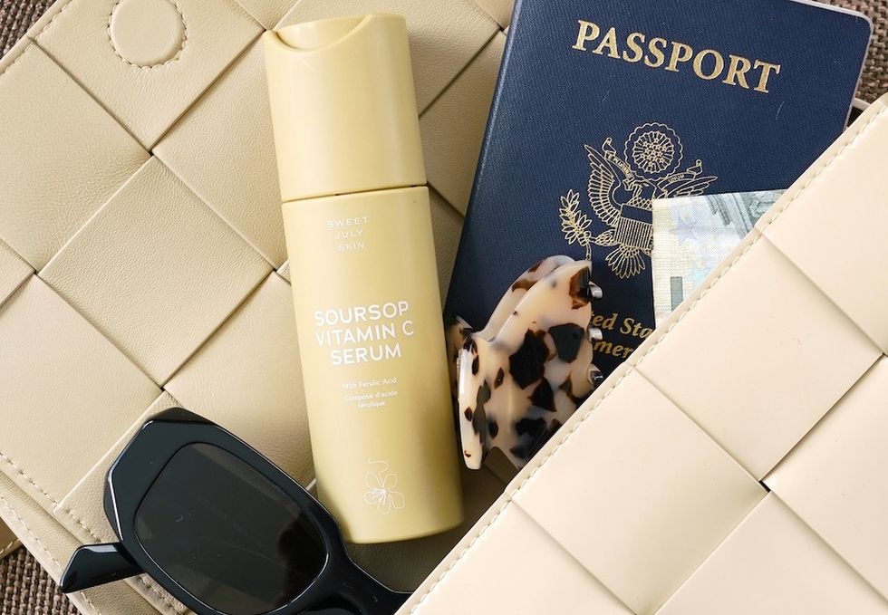 a bag with sunglasses, vitamin c serum, a claw clip, and a passport spilling out