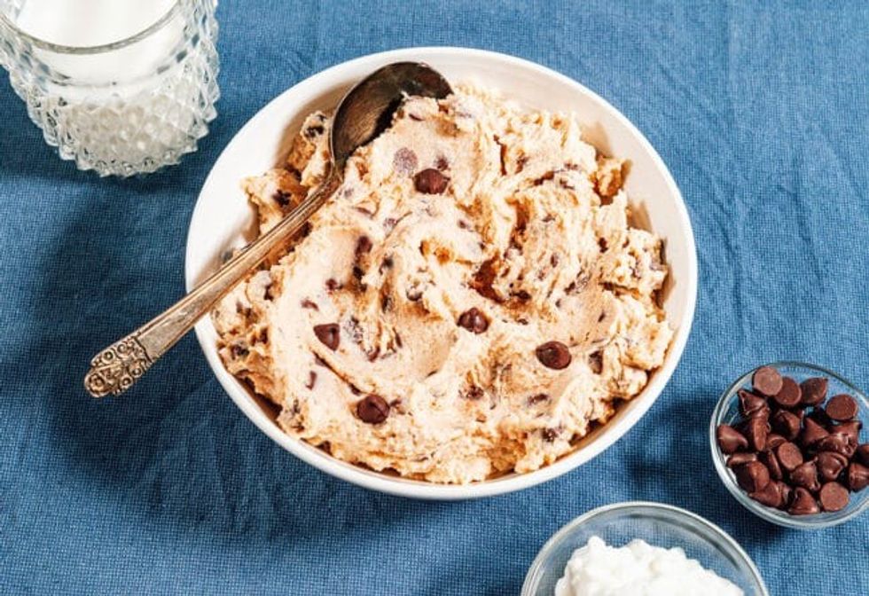 A bowl full of cottage cheese cookie dough sits on top of a blue cloth, next to chocolate chips.