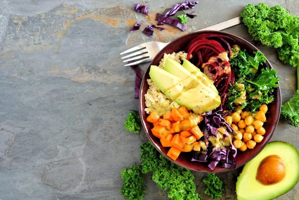 A bowl full of fresh vegetables and quinoa rests on a slate background