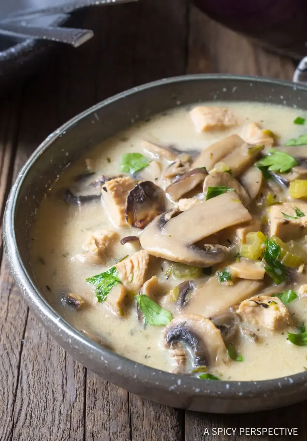 A bowl of chicken mushroom soup sits on top of a wooden table.
