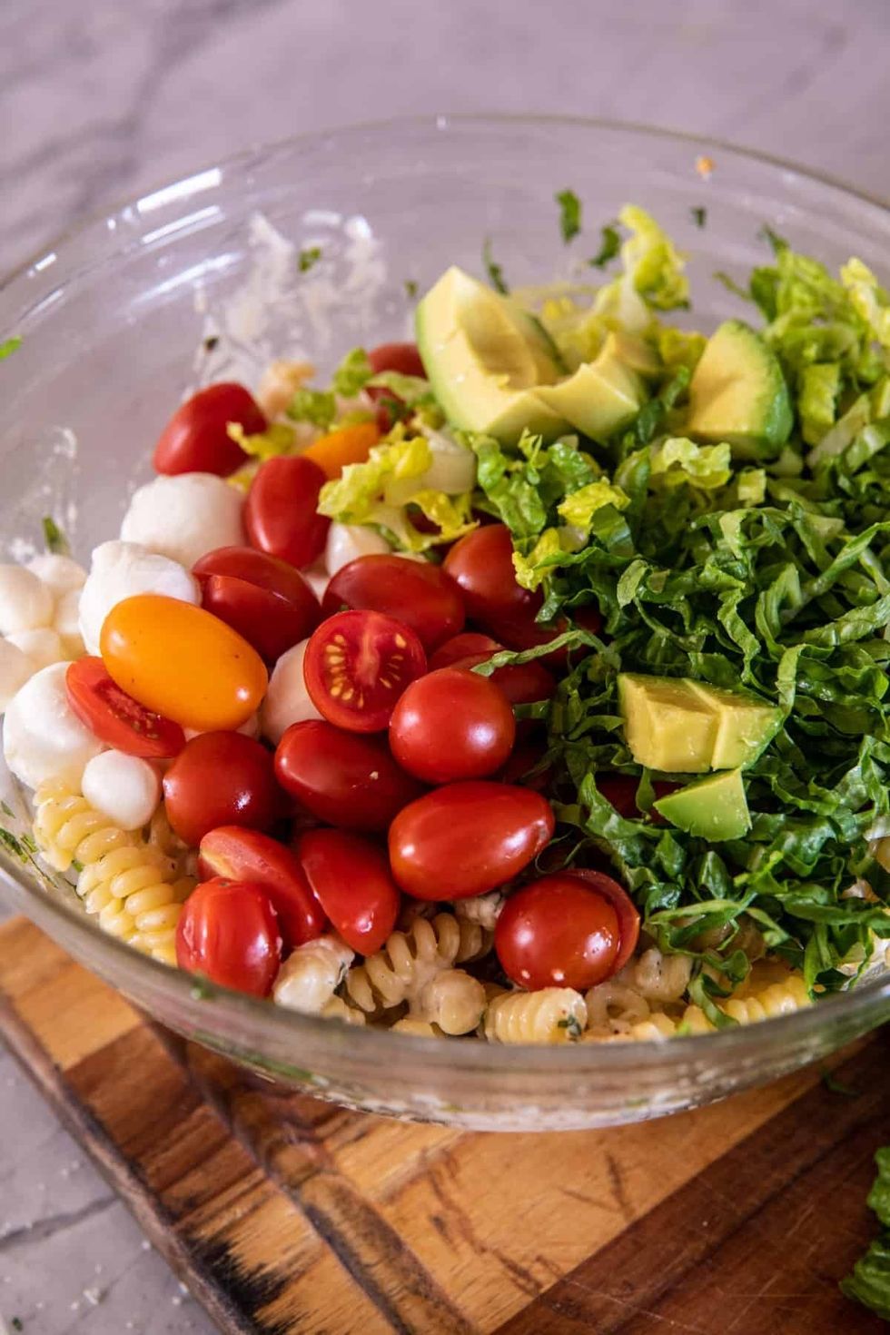 A bowl of colorful Caprese caesar pasta salad sits on a wooden tray.