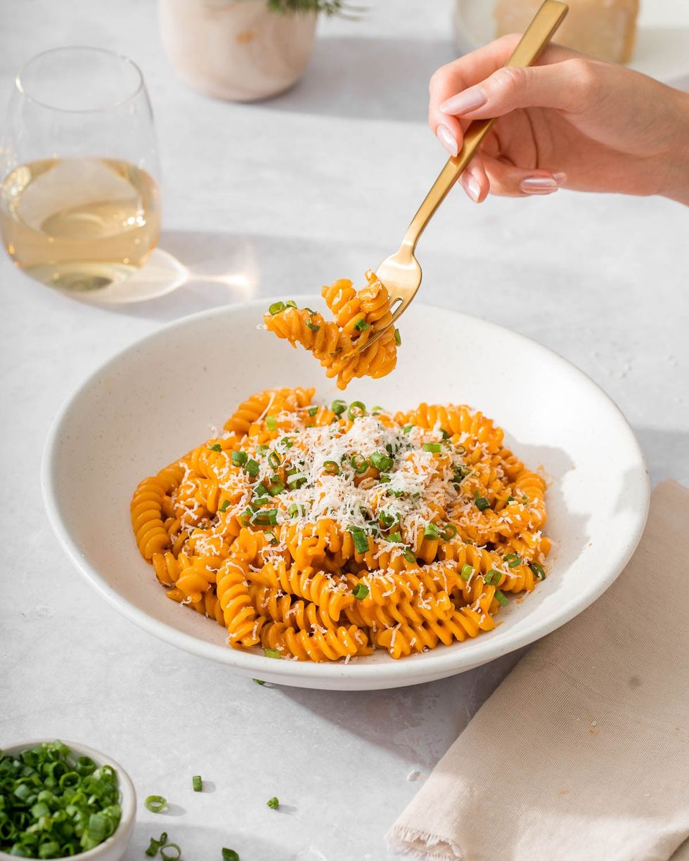 A bowl of Gochujang pasta is sitting next to a cloth and a bowl of green onions.