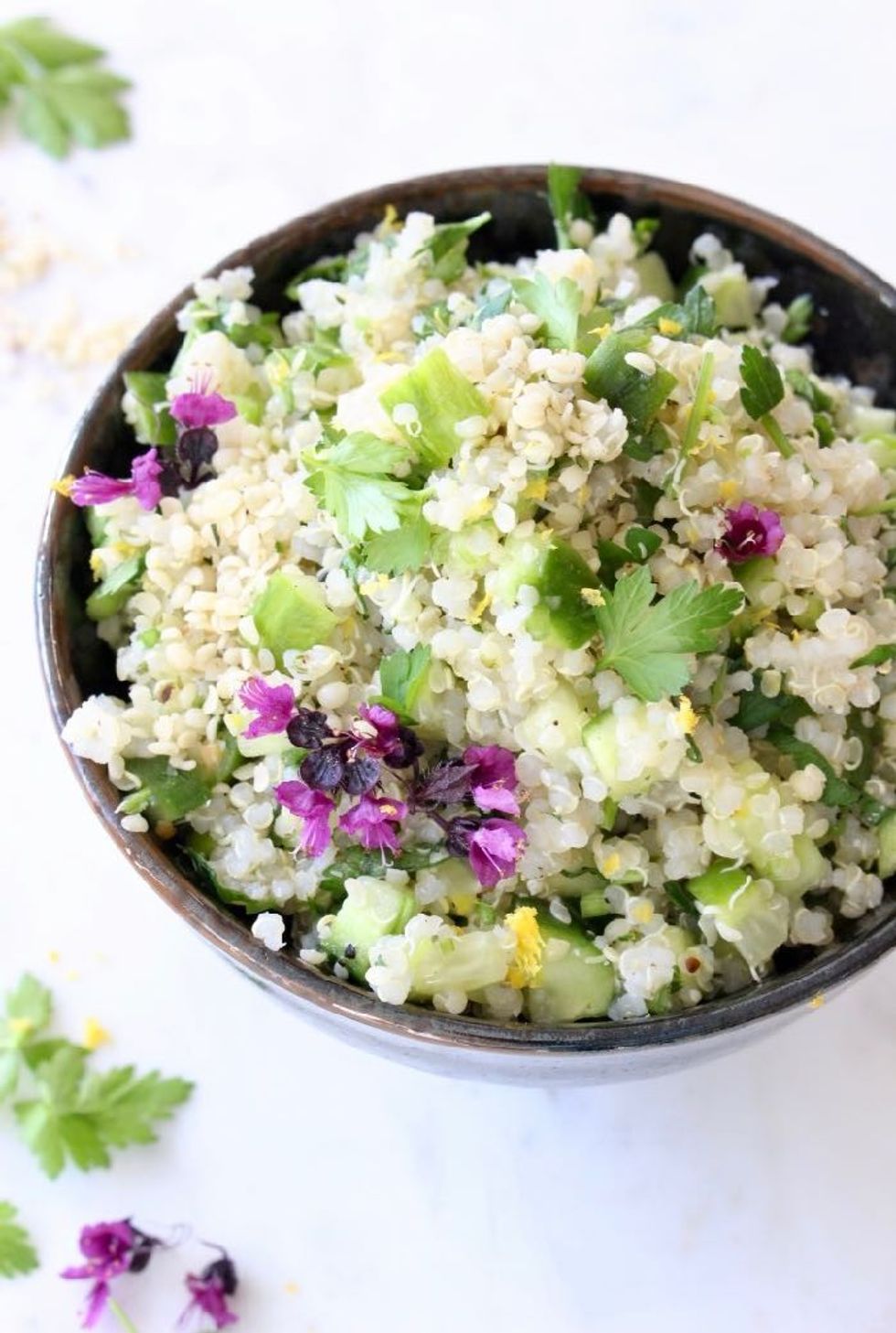 A bowl of lemon quinoa cucumber salad is garnished with small purple flowers.