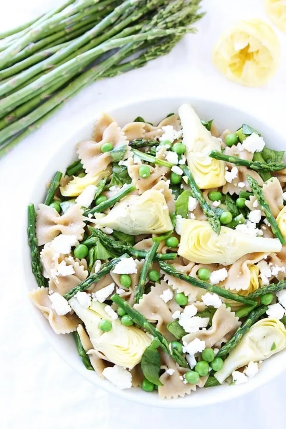 A bowl of spring pasta salad with penne is sitting on a white surface.