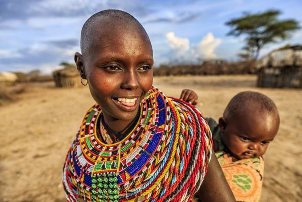 A brightly dressed woman smiles as she carries her baby on her back