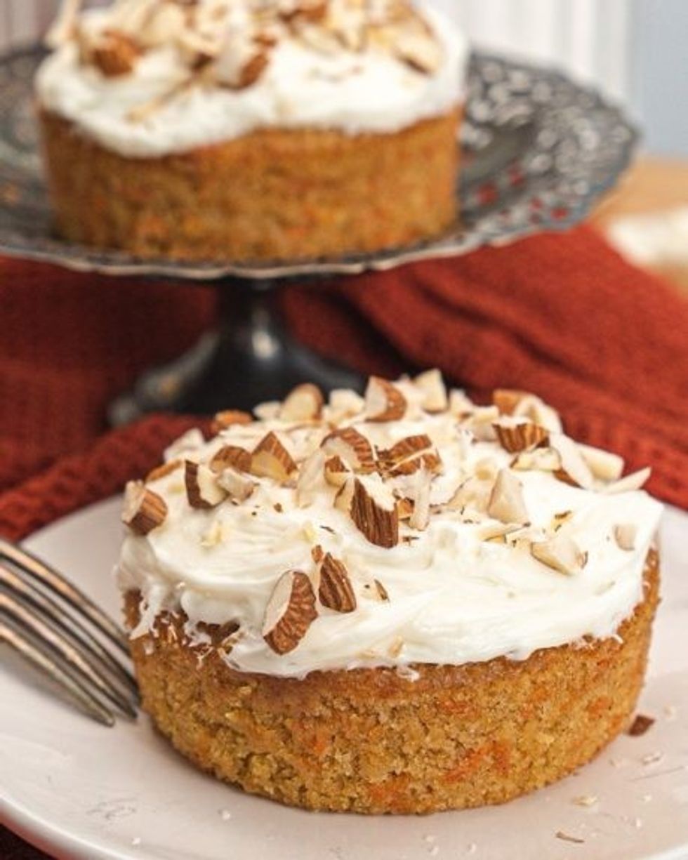A carrot cake recipe with almonds on top sits on a plate.
