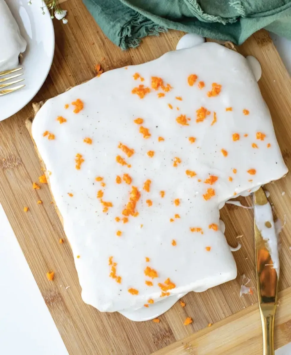 A carrot cake with a slice cut out sits on a wooden board.