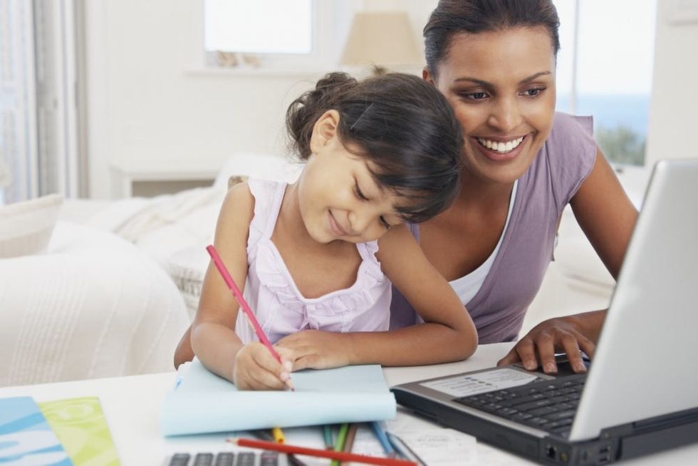 A child draws while her mother works on a laptop