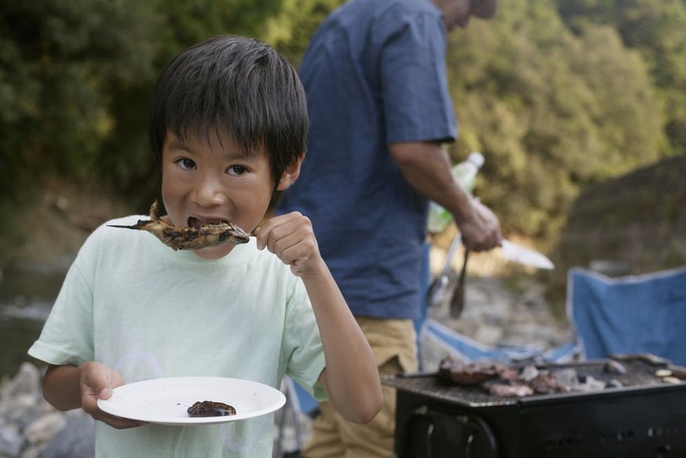 A child eats grilled fish at a picnic