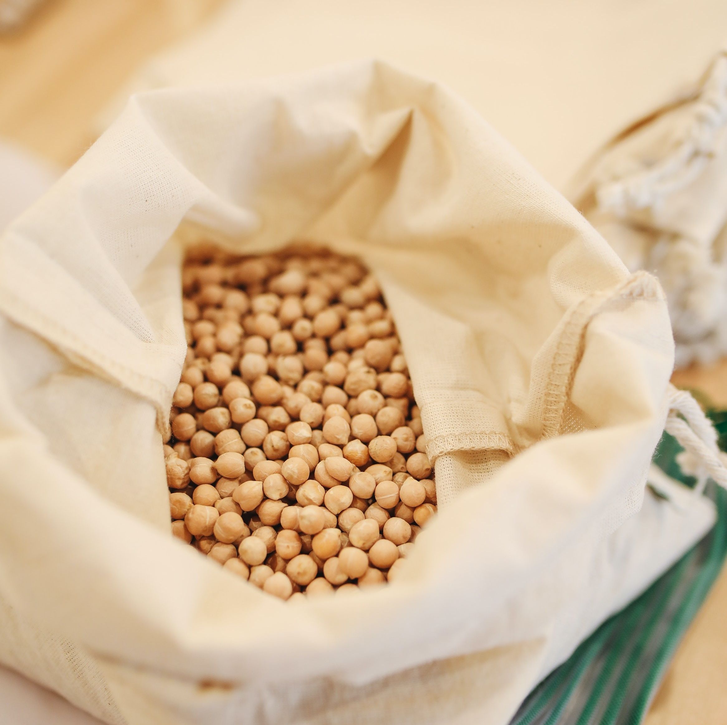 A cloth bag of chickpeas sits on a wooden surface.