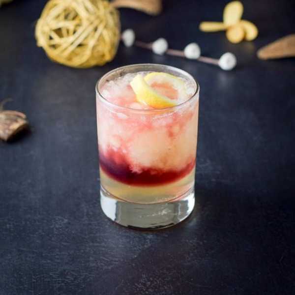 A cocktail with layered colors and a lemon twist on a dark background.