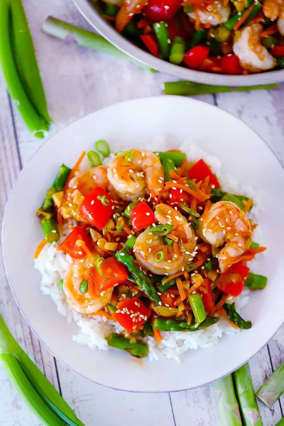 A colorful bowl of shrimp stir fry is on a white table.