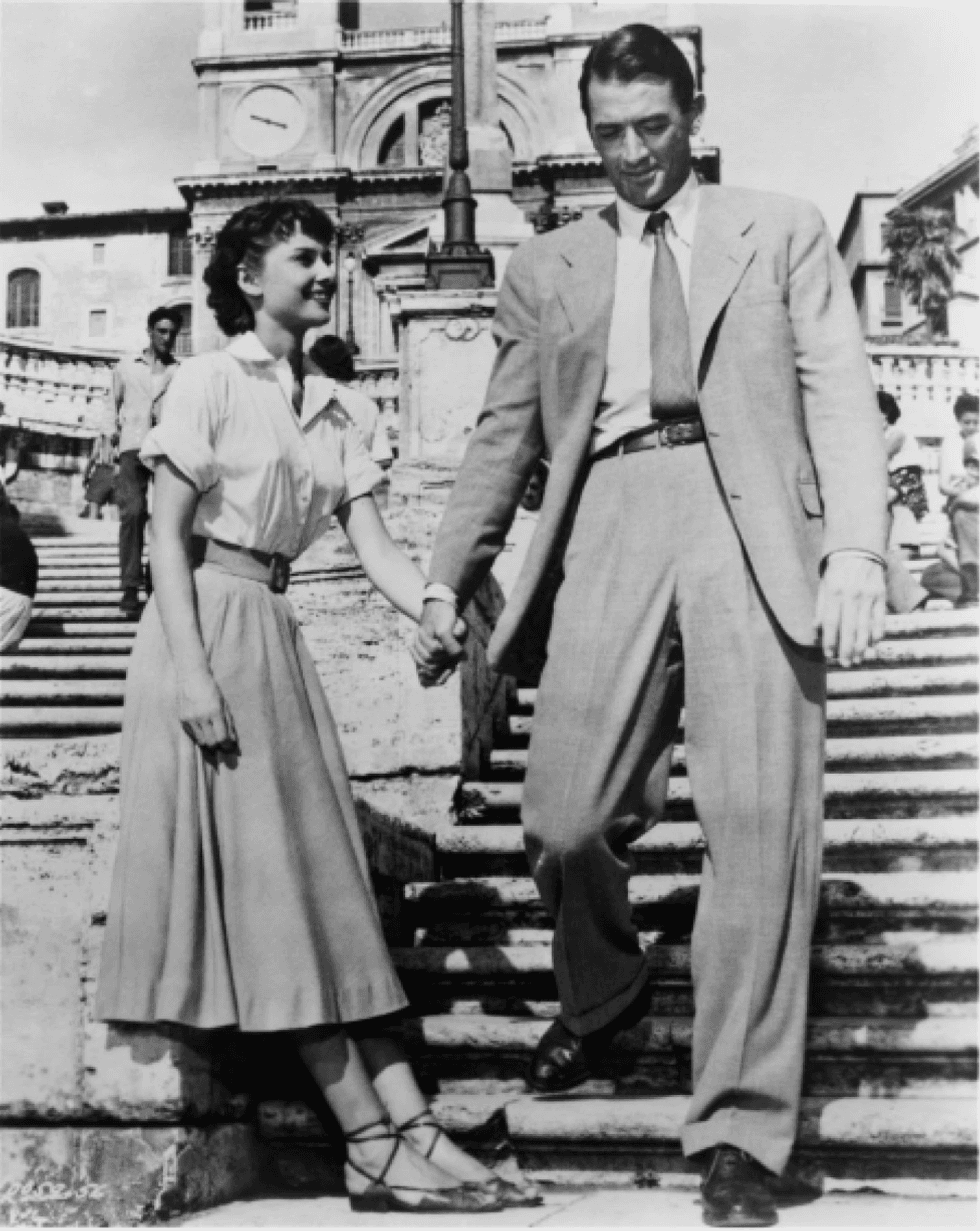 A couple holding hands, walking down steps in elegant 1950s attire.