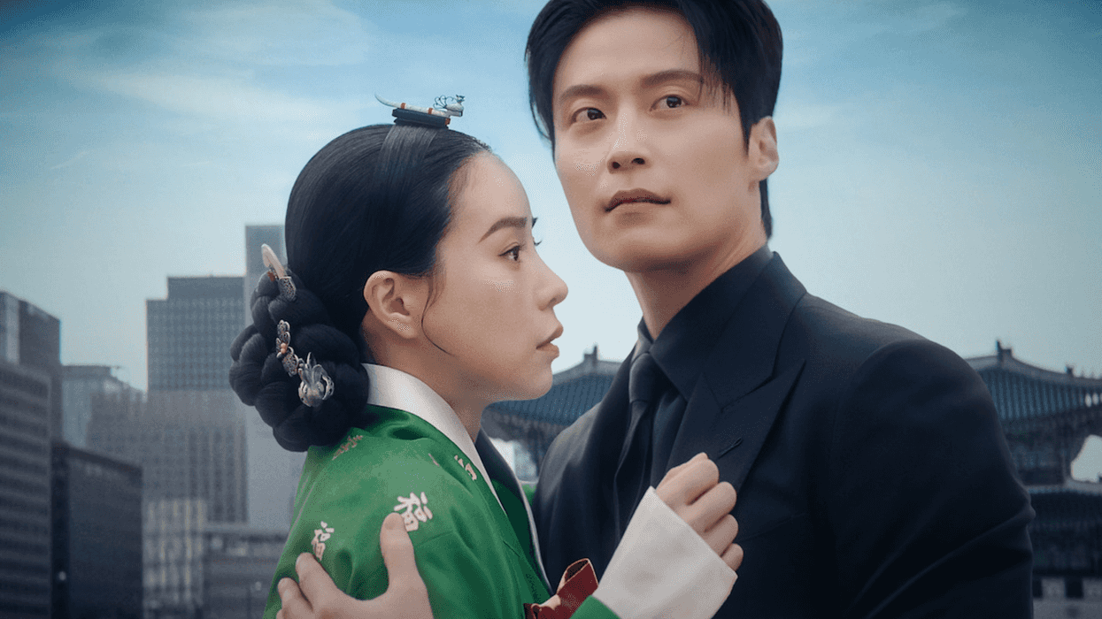 A couple in traditional and modern attire embrace against a cityscape and historical backdrop.
