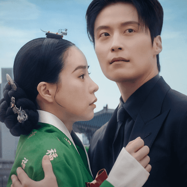 A couple in traditional and modern attire embrace against a cityscape and historical backdrop.