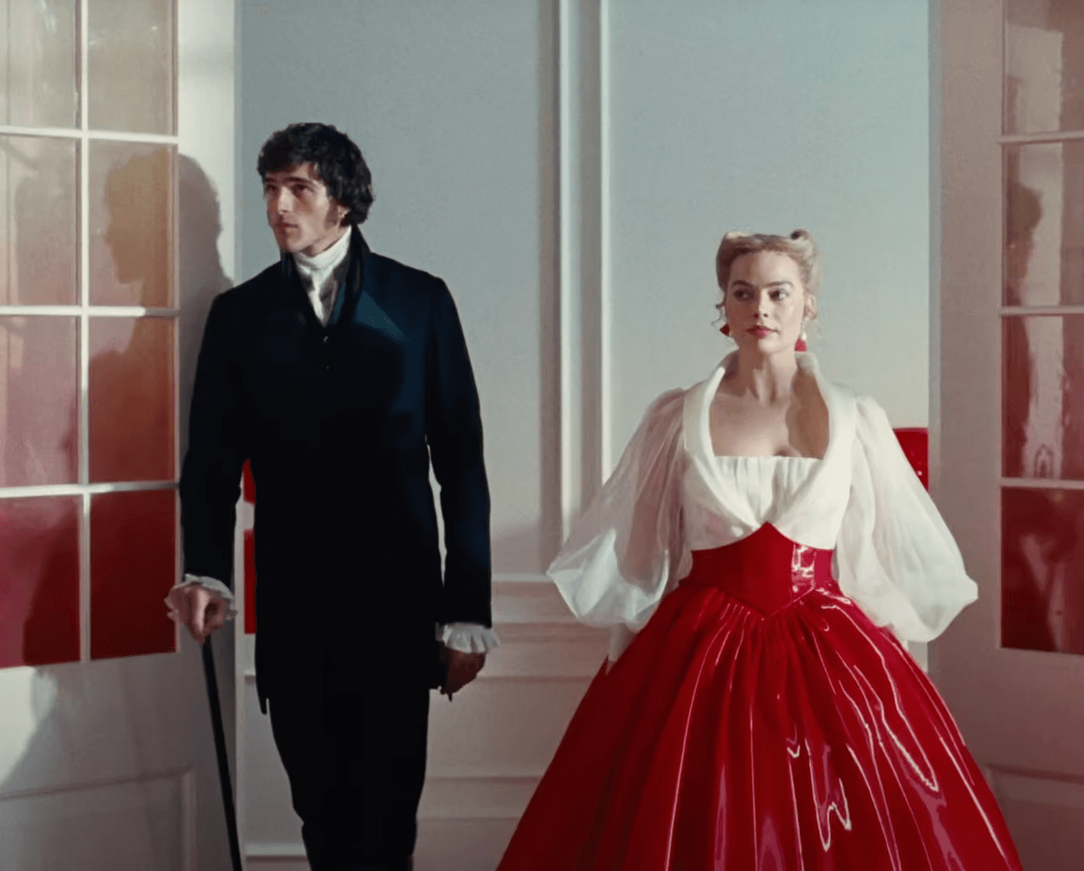 A couple in vintage attire pose in a brightly lit, elegant room with red accents.