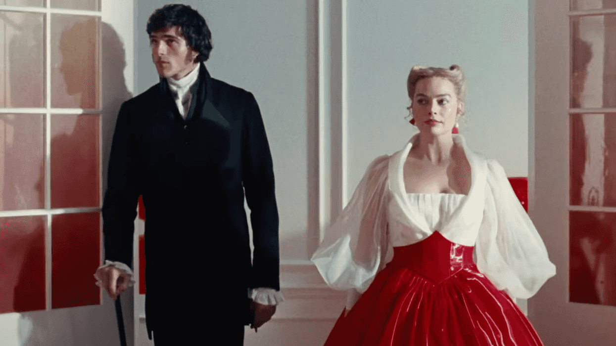 A couple in vintage attire pose in a brightly lit, elegant room with red accents.