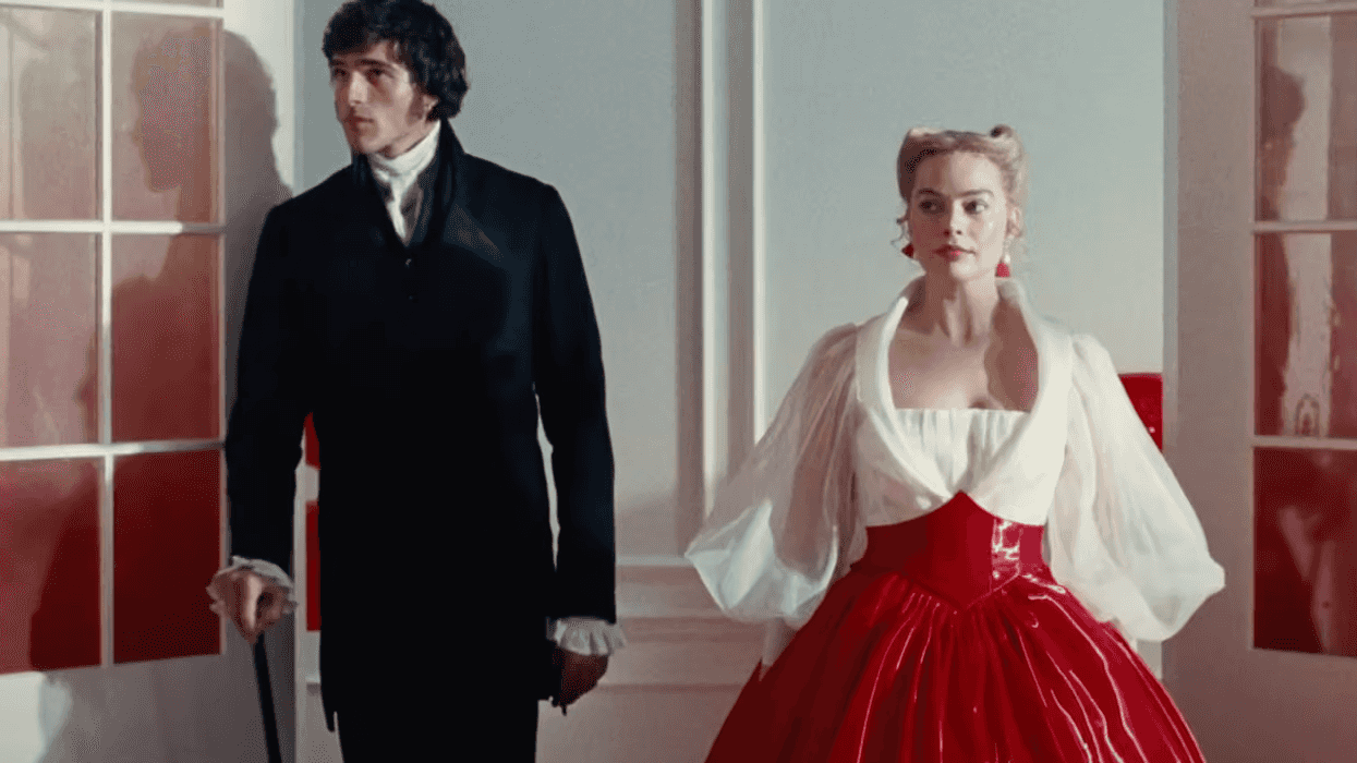 A couple in vintage attire pose in a brightly lit, elegant room with red accents.