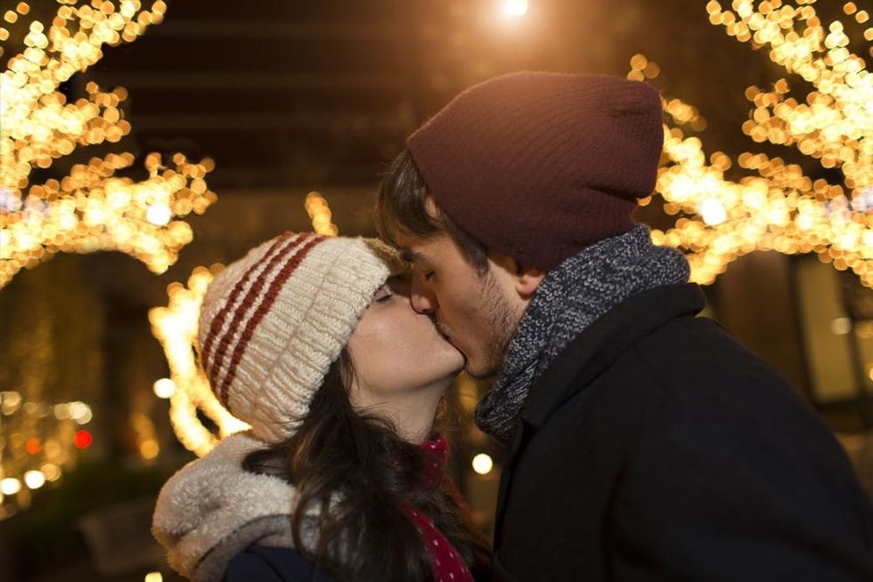 A couple kisses in front of holiday lights