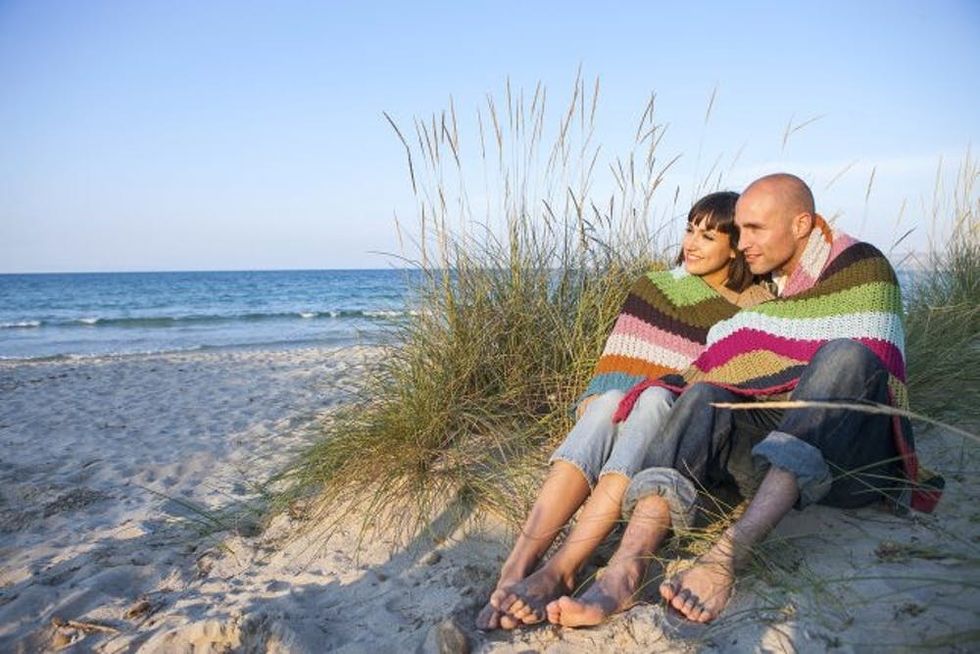 A couple sits together watching the ocean under a colorful blanket