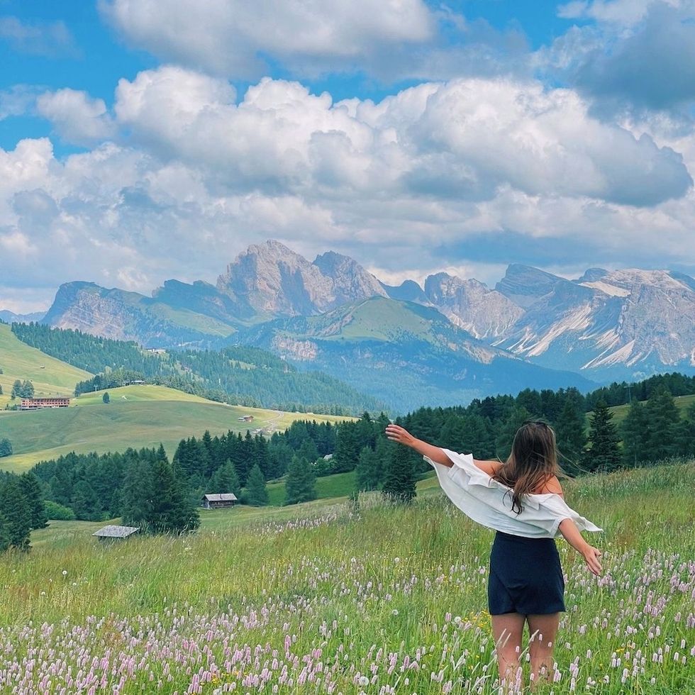 a girl in a field looking at the mountains with her arms wide open