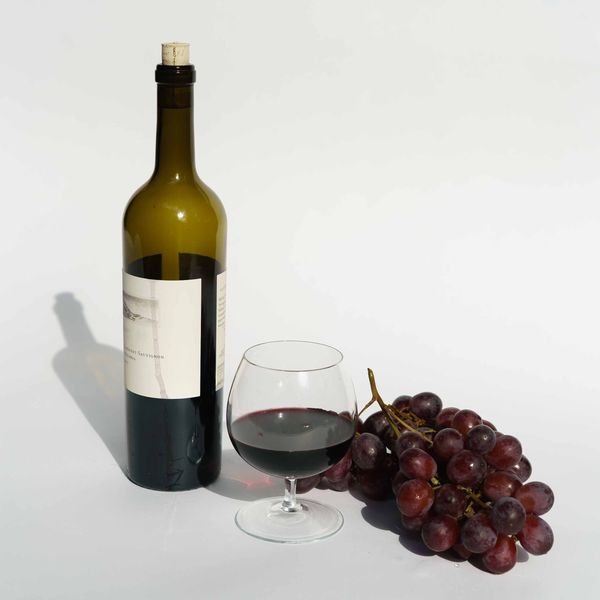 a glass of red wine with red grapes and a wine bottle