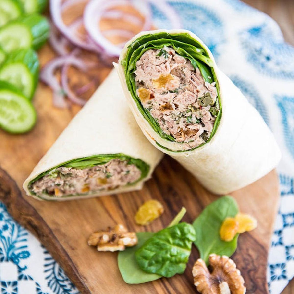 A healthy wrap filled with chicken salad on a wood cutting board with spinach and walnuts.