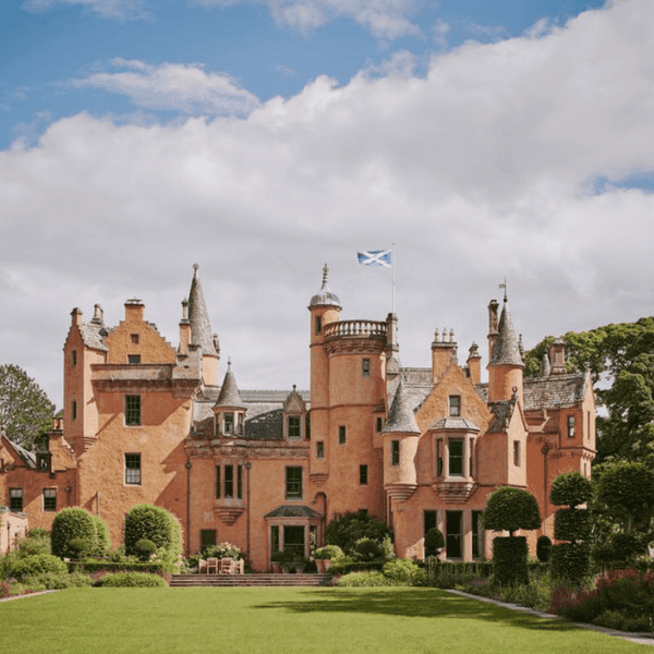 A historic castle with turrets and the Scottish flag, surrounded by greenery.