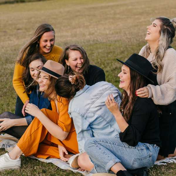 A joyful group of friends laughing together on a picnic blanket in a grassy field.