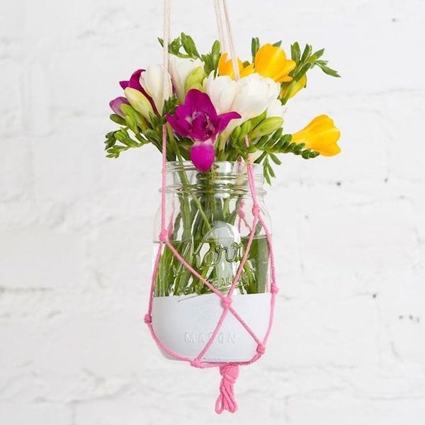 A large jar painted white in a pink macrame knit basket is just one of 56 DIY mason jar crafts to explore.