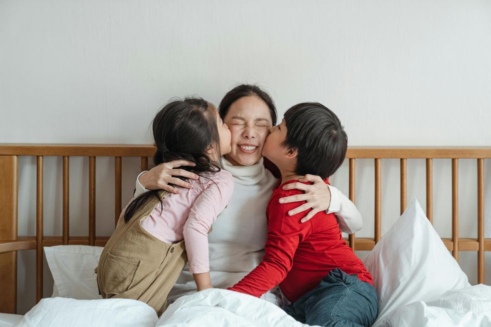 a little girl and a little boy kissing their mom on the cheeks