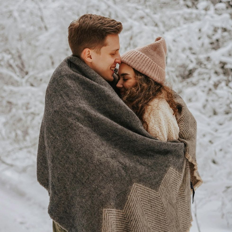 a man and a woman hugging in a blanket in the winter snow