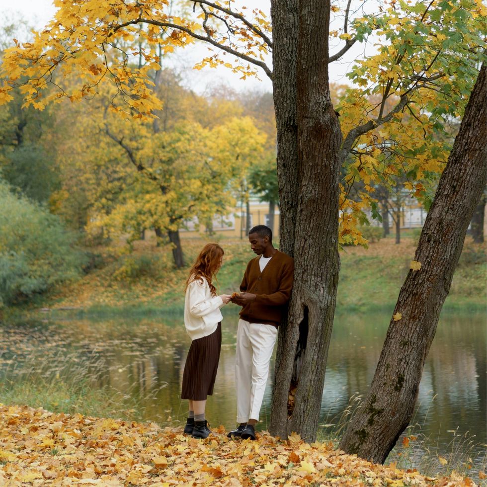 a man and a woman talking next to a tree by a river in the fall