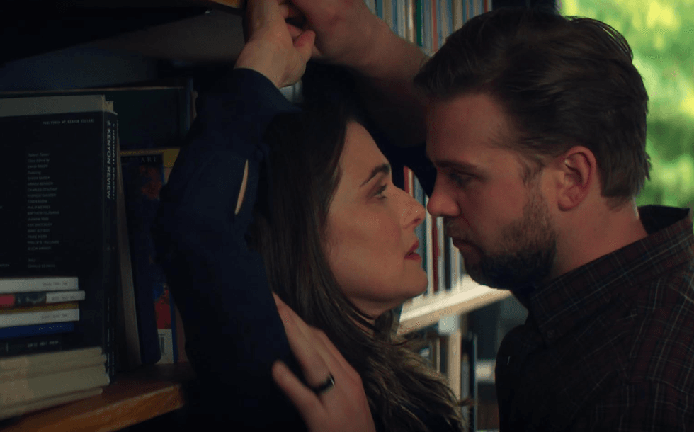 A man and woman share an intense gaze in a library setting.