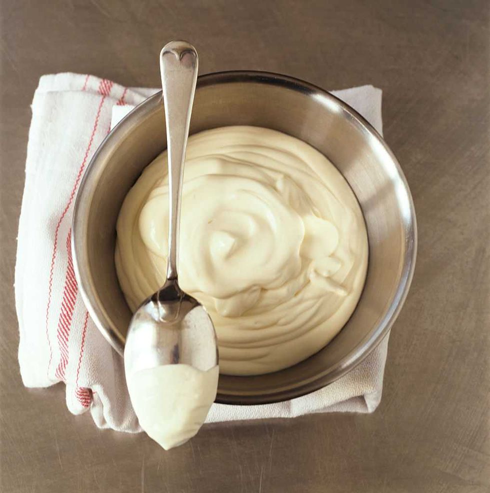 A metal bowl of creamy mayonnaise with a spoon on a cloth napkin.