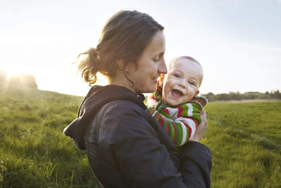 A mother holds a laughing baby in a field
