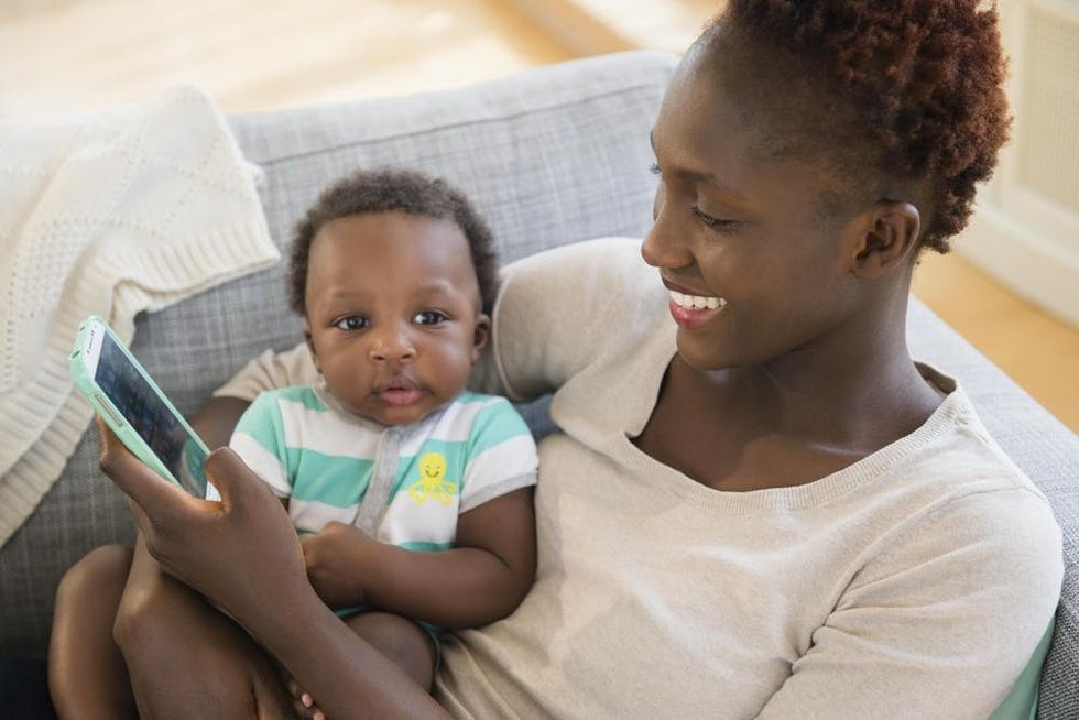 A mother uses a cell phone while holding her baby