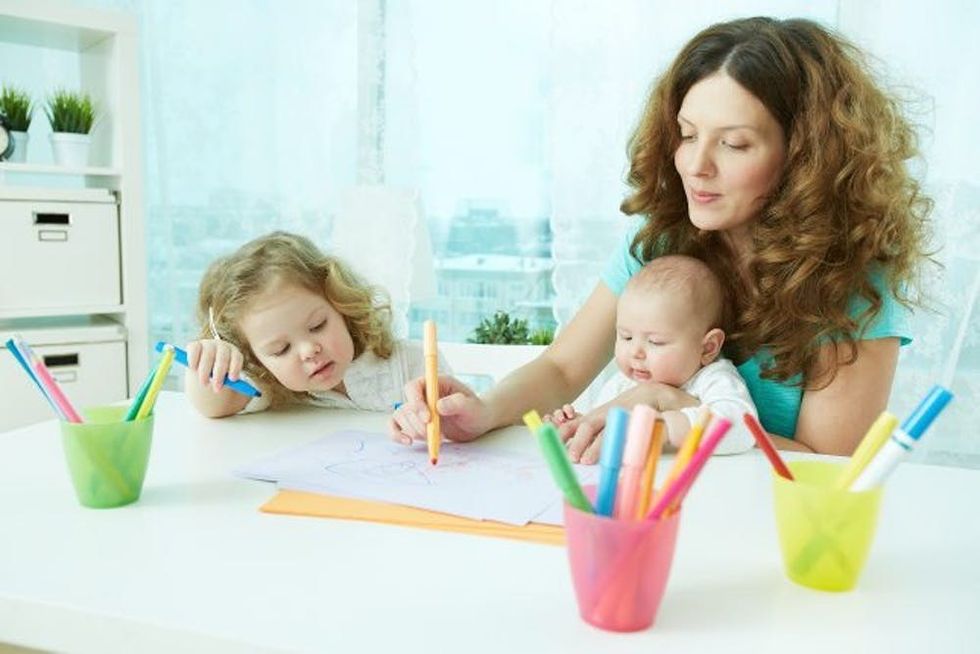 A nanny colors with a baby and a young child