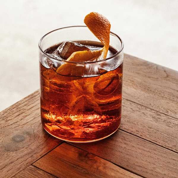A Negroni cocktail with ice and an orange twist on a wooden table.