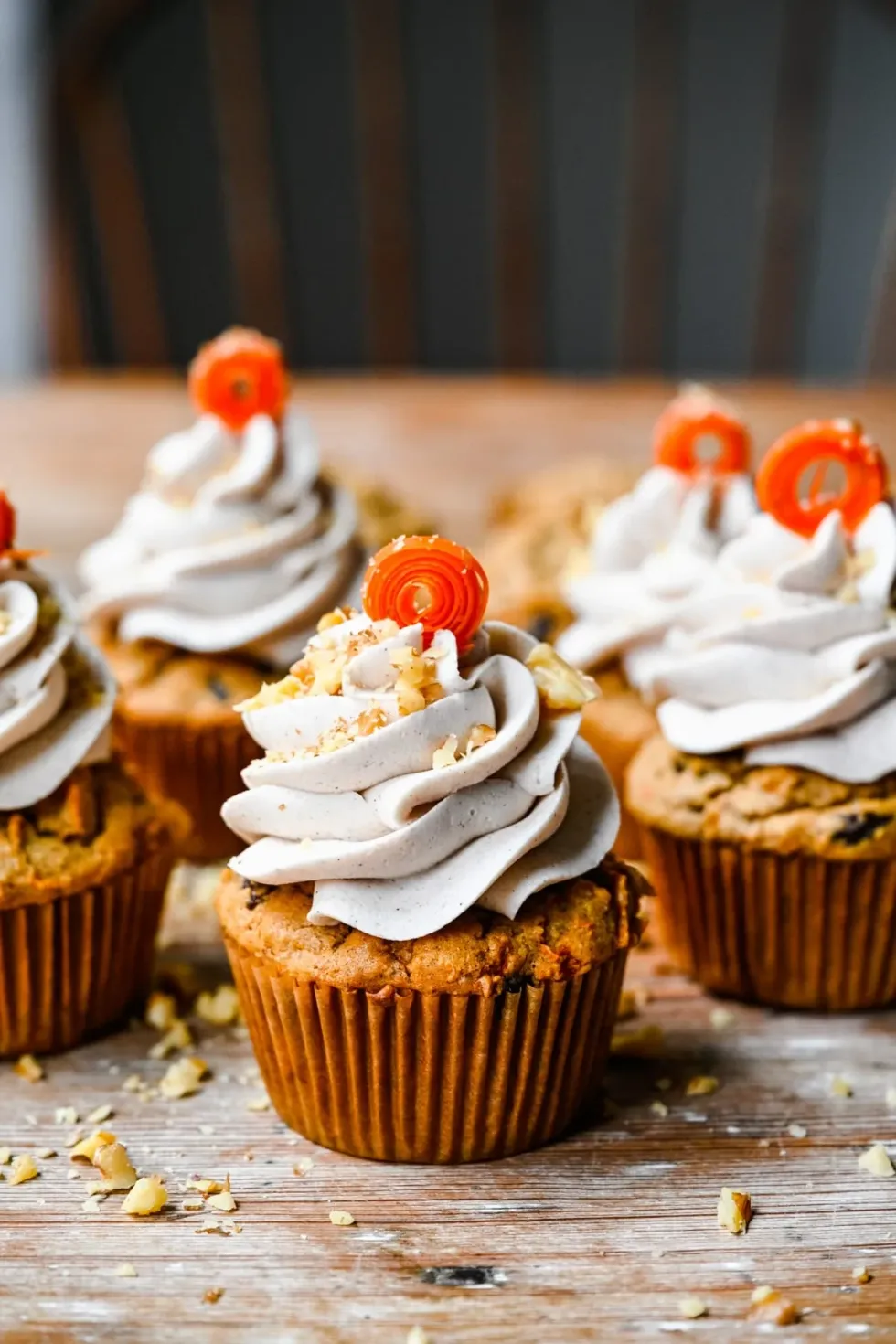A number of carrot cupcakes sit on a wooden table.