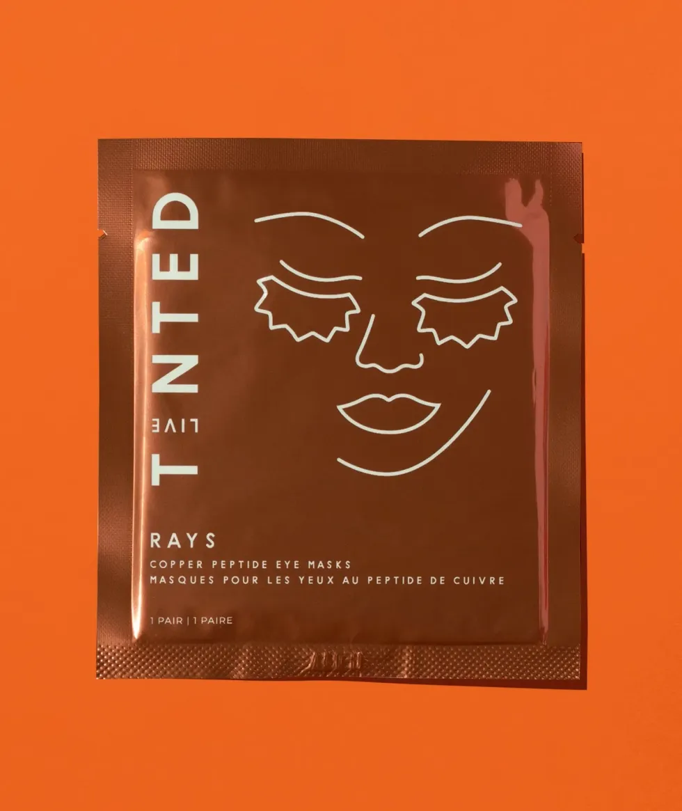 A package of copper eye masks with a face on it is in front of an orange background.