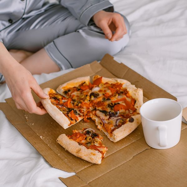 a person in bed eating pizza out of a box