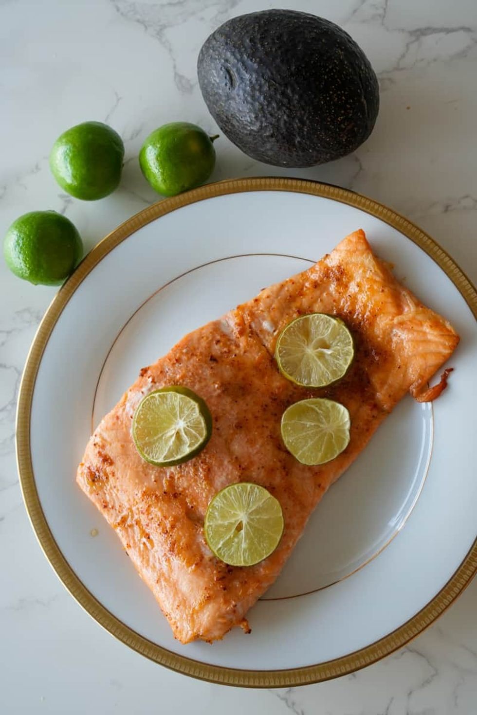 A piece of spicy salmon sits on a white plate with gold trim.