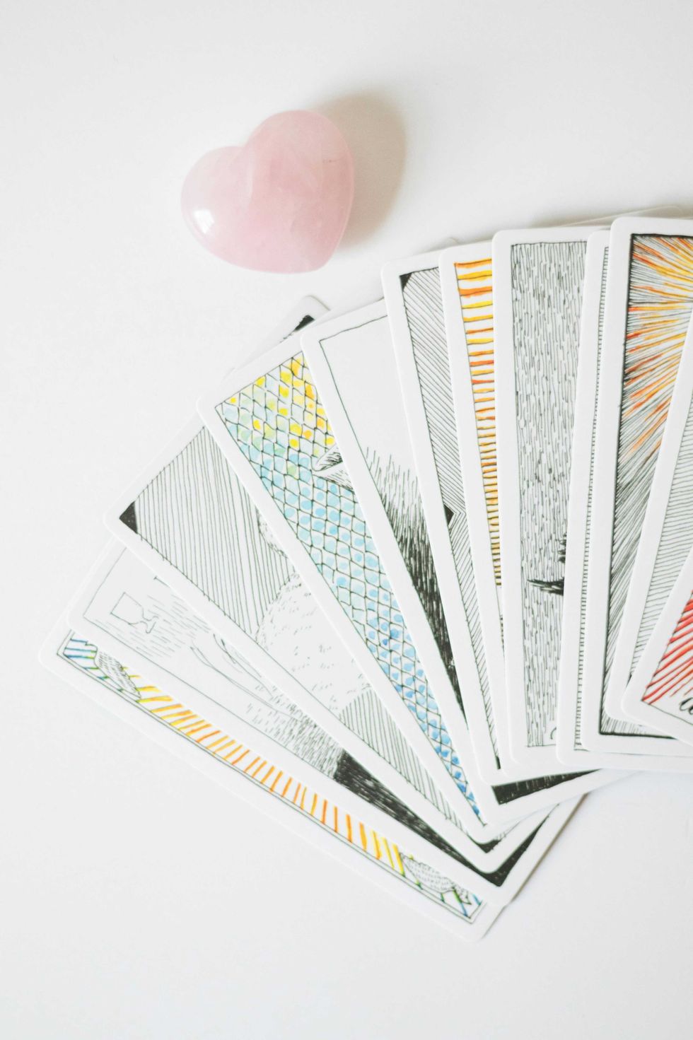 A pink heart-shaped stone above a fanned-out set of illustrated tarot cards on a white background.