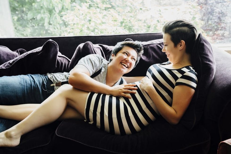 A pregnant couple cuddles on a sofa
